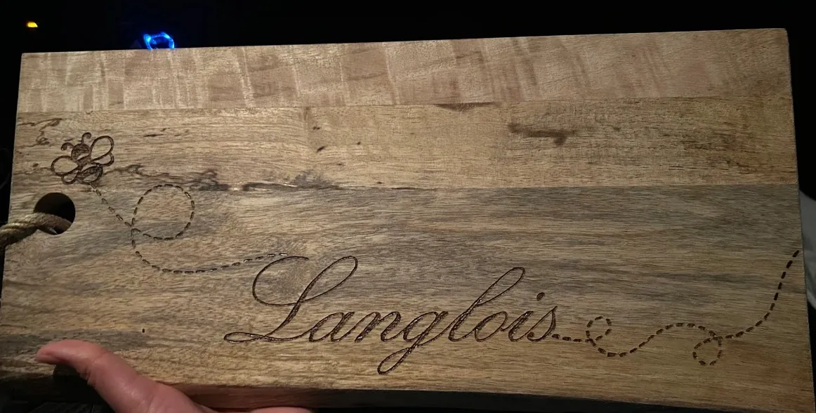 Wooden board wood-burned by hand with the name Langlois and a bee with a dotted flight path